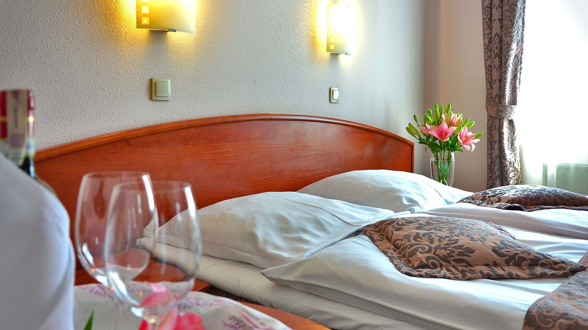 NürnbergMesse - Nahgelegene Hotels und exklusive Shoppingerlebnisse - sehr ordentliches Hotelbett mit Blumen auf dem Nachttisch und Weingläsern auf dem Esstisch