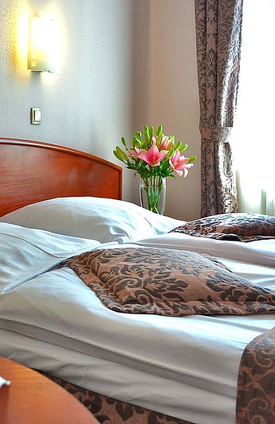 Pauschalen für eine Woche in Mittelfranken - im Hotelzimmer von Gardinen durchleuchtet; Weingläser auf Tisch und Blumenstrauß auf Nachttisch