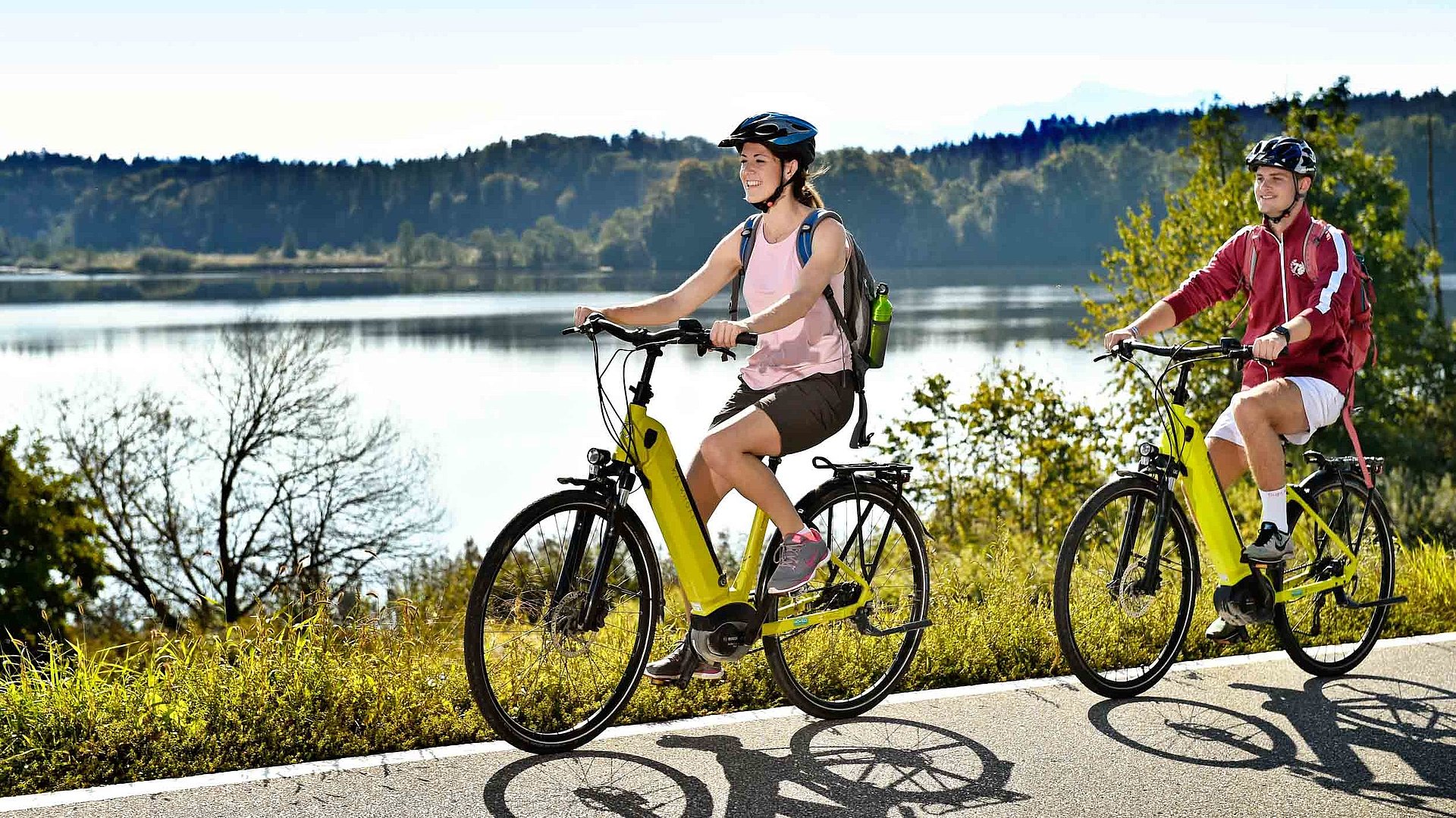 Radfahren und Radwandern in Franken - zwei Partner auf E-Bike fahren am See entlang; Waldgebiet im Hintergrund