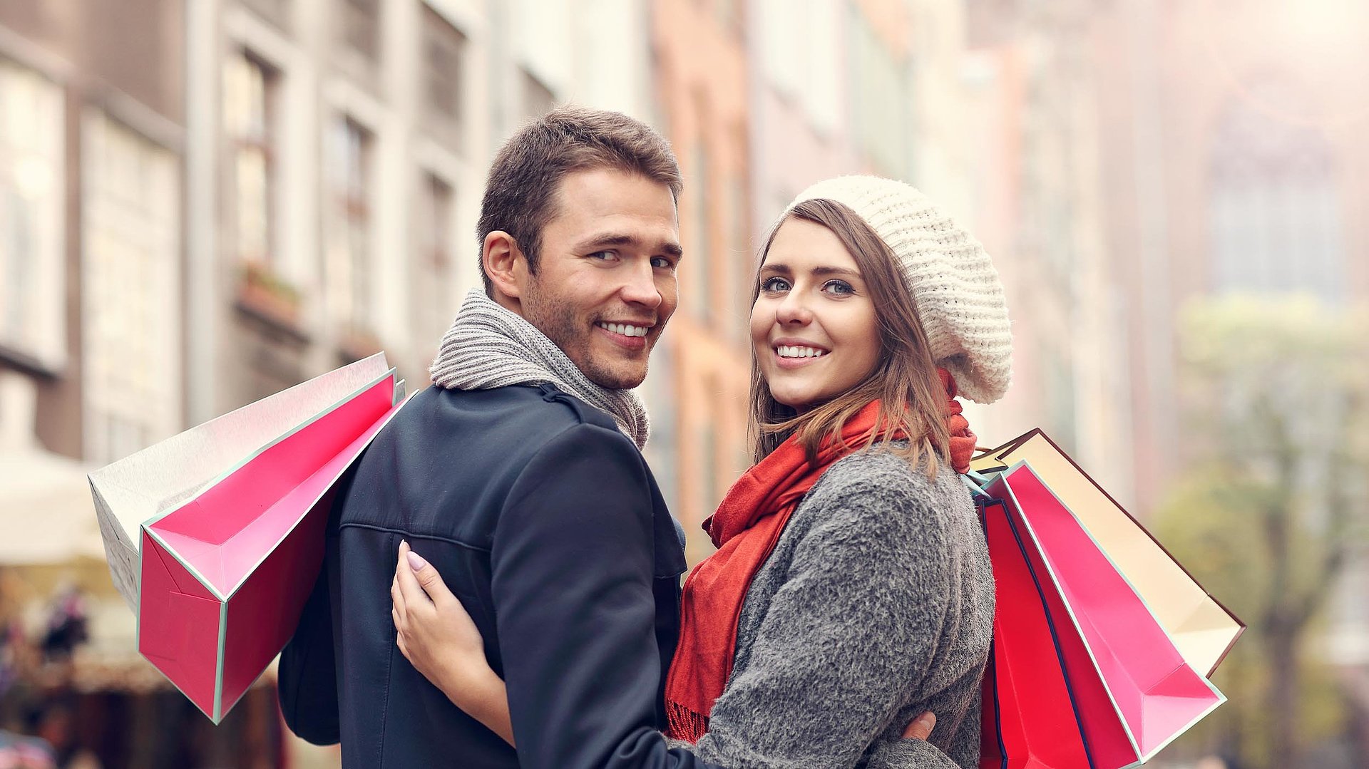 Einkaufen im Fichtelgebirge - Paar mit rosa und weißen Einkaufstüten vor Stadthäusern lächeln in die Kamera