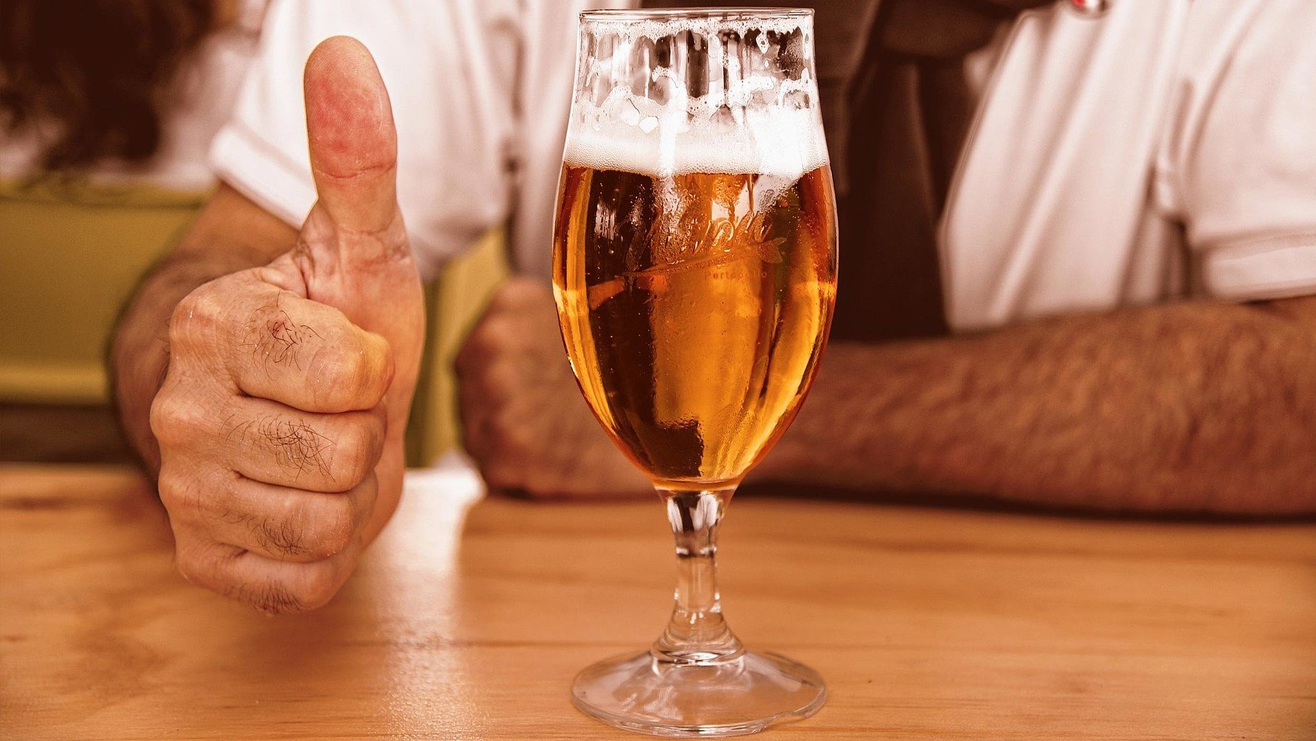 Biergarten in Franken - fast volles Bier auf Holztisch; Mann im Hintergrund zeigt Daumen Hoch