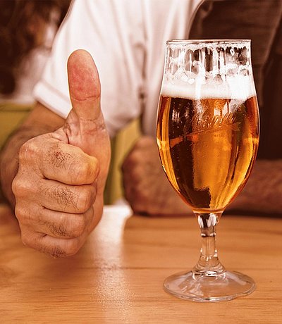 Brauereigasthöfe in Franken - fast volles Bier auf Holztisch; Mann im Hintergrund zeigt Daumen Hoch
