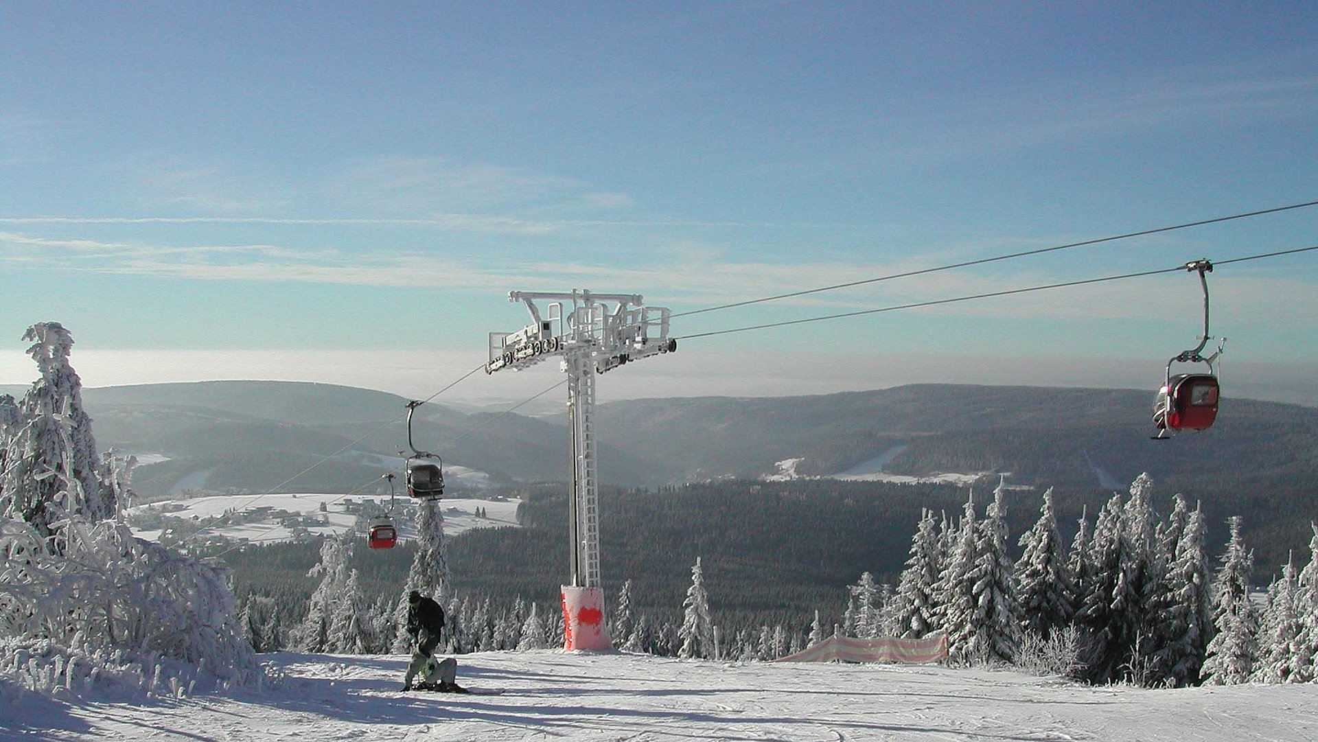 Wintersport-Unterkünfte im Fichtelgebirge - Wintersportfläche umgeben von Bäumen mit mittig gelegener Seilbahn, Bild mit Blick auf Hügel und Horizont unter blauem Himmel