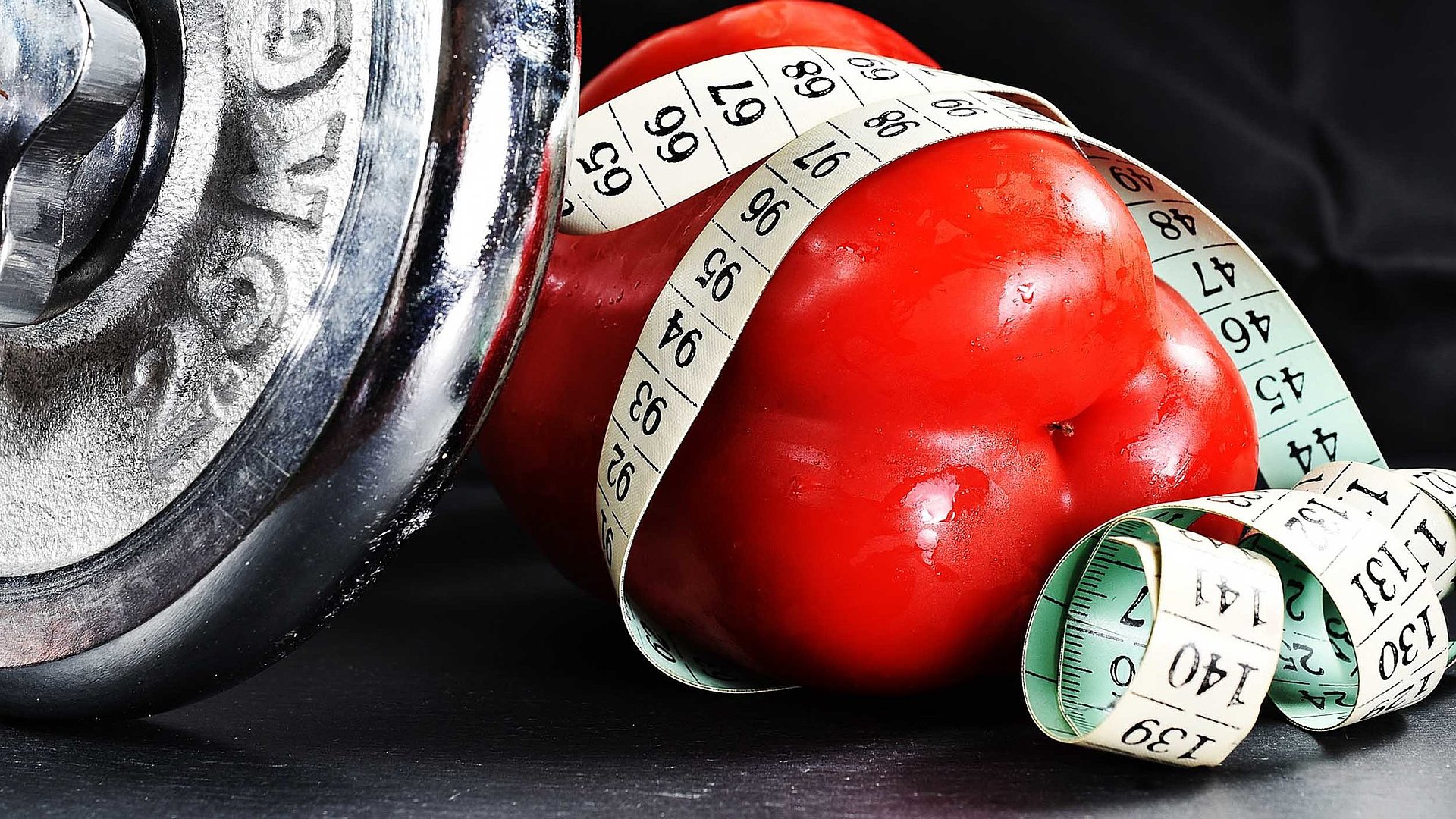 Fitness und Gesundheit im Oberallgäu - Fokus auf eine rote Paprika, die teilweise von einem Maßband umwickelt ist; Daneben eine 2.5kg-Hantel