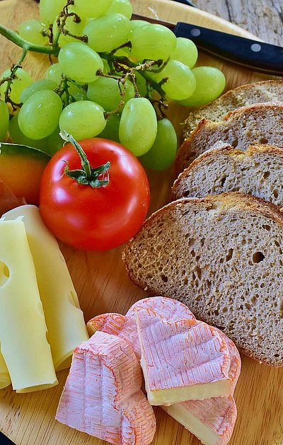 Brotzeit in Ostbayern - rundes Holzbrett mit Brot, französischem Käse, Scheibenkäse, Tomate und Weintrauben