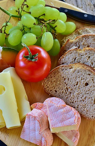 Frühstück in Nürnberg - rundes Holzbrett mit Brot, französischem Käse, Scheibenkäse, Tomate und Weintrauben  