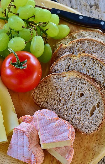 Brotzeit in Oberfranken - rundes Holzbrett mit Brot, französischem Käse, Scheibenkäse, Tomate und Weintrauben