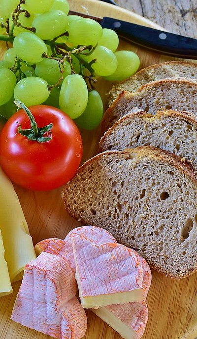 Brotzeit in Mittelfranken - rundes Holzbrett mit Brot, französischem Käse, Scheibenkäse, Tomate und Weintrauben