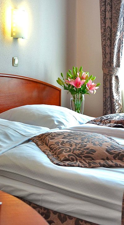 Pensionen und Gasthöfe für Gruppen in Mittelfranken - im Hotelzimmer von Gardinen durchleuchtet; Weingläser auf Tisch und Blumenstrauß auf Nachttisch