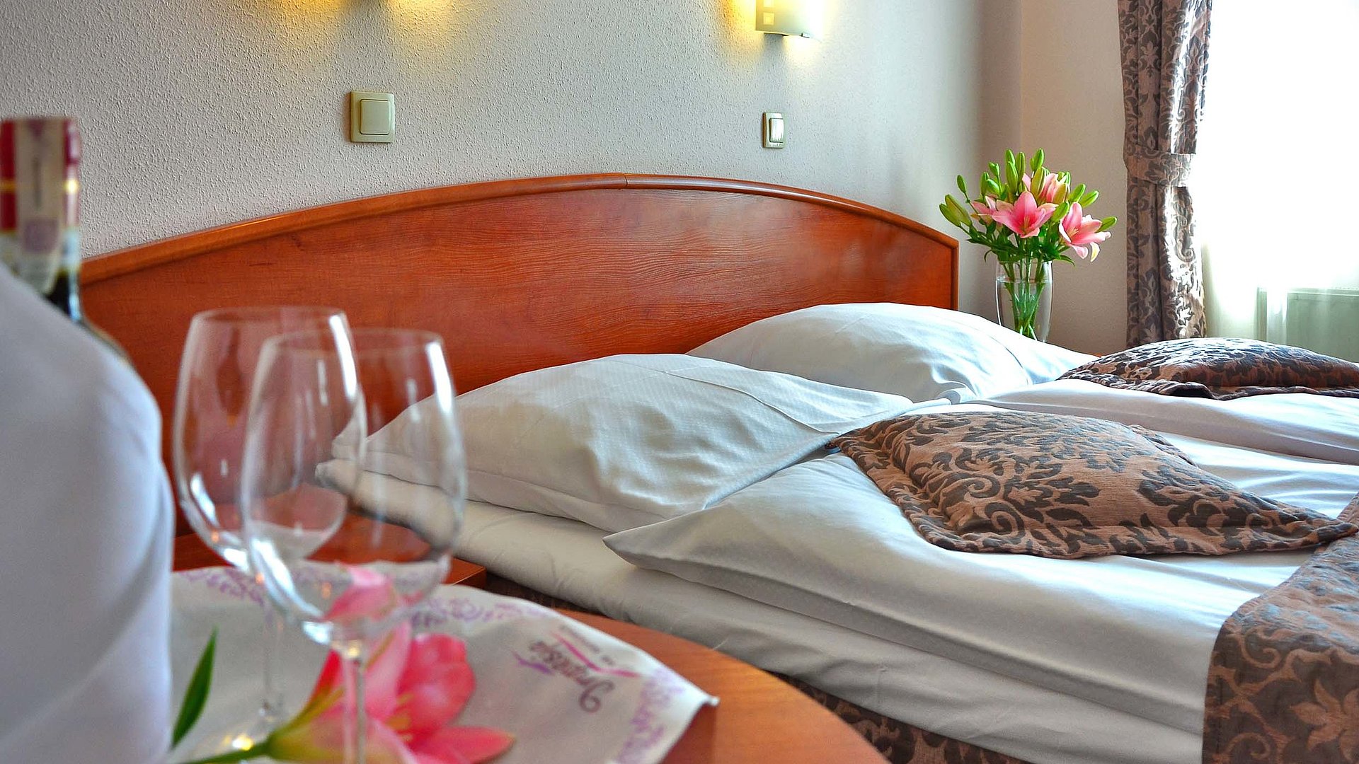 Pensionen und Gasthöfe für Gruppen in Mittelfranken - im Hotelzimmer von Gardinen durchleuchtet; Weingläser auf Tisch und Blumenstrauß auf Nachttisch 