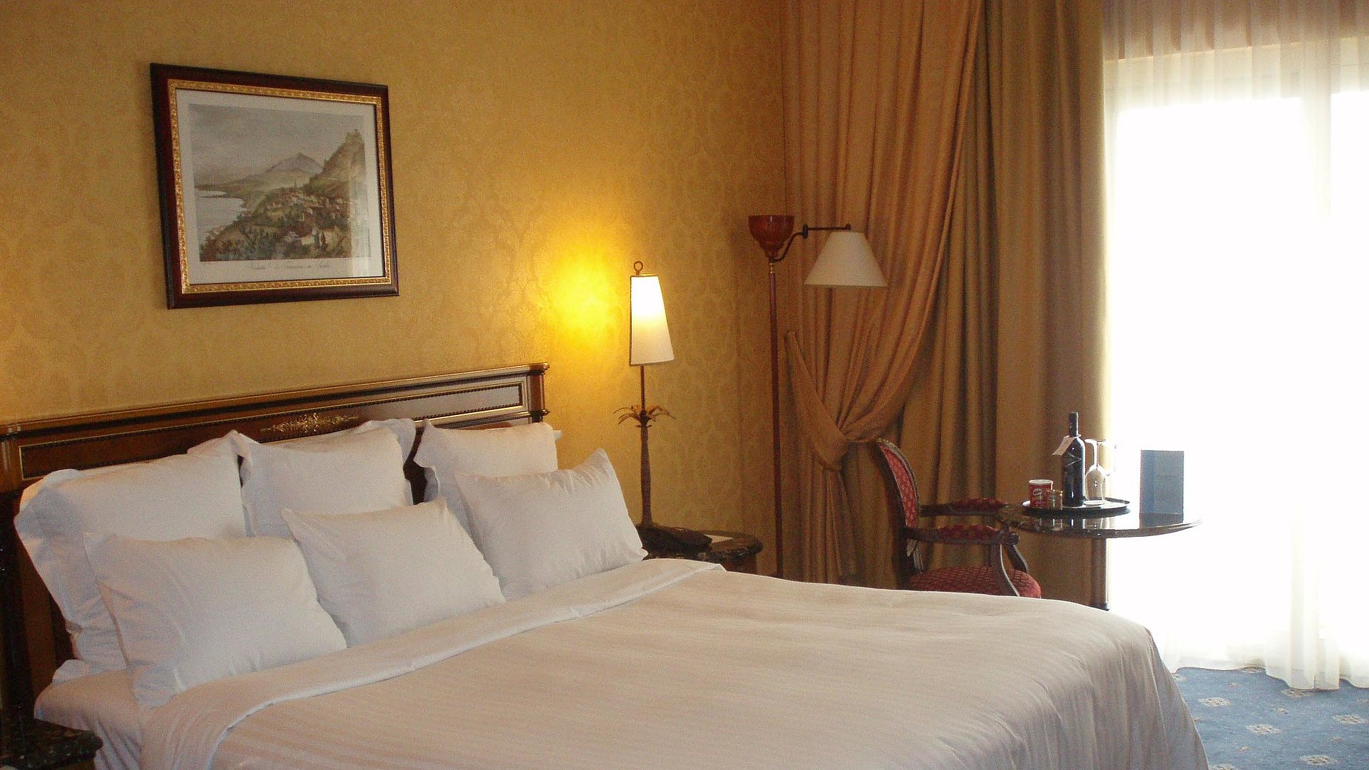 Pauschalangebote für eine Woche in Unterfranken - sehr ordentliches Hotelzimmer mit großem Bett und warmer Nachtlampe wird durch weiße Gardinen durchleuchtet 