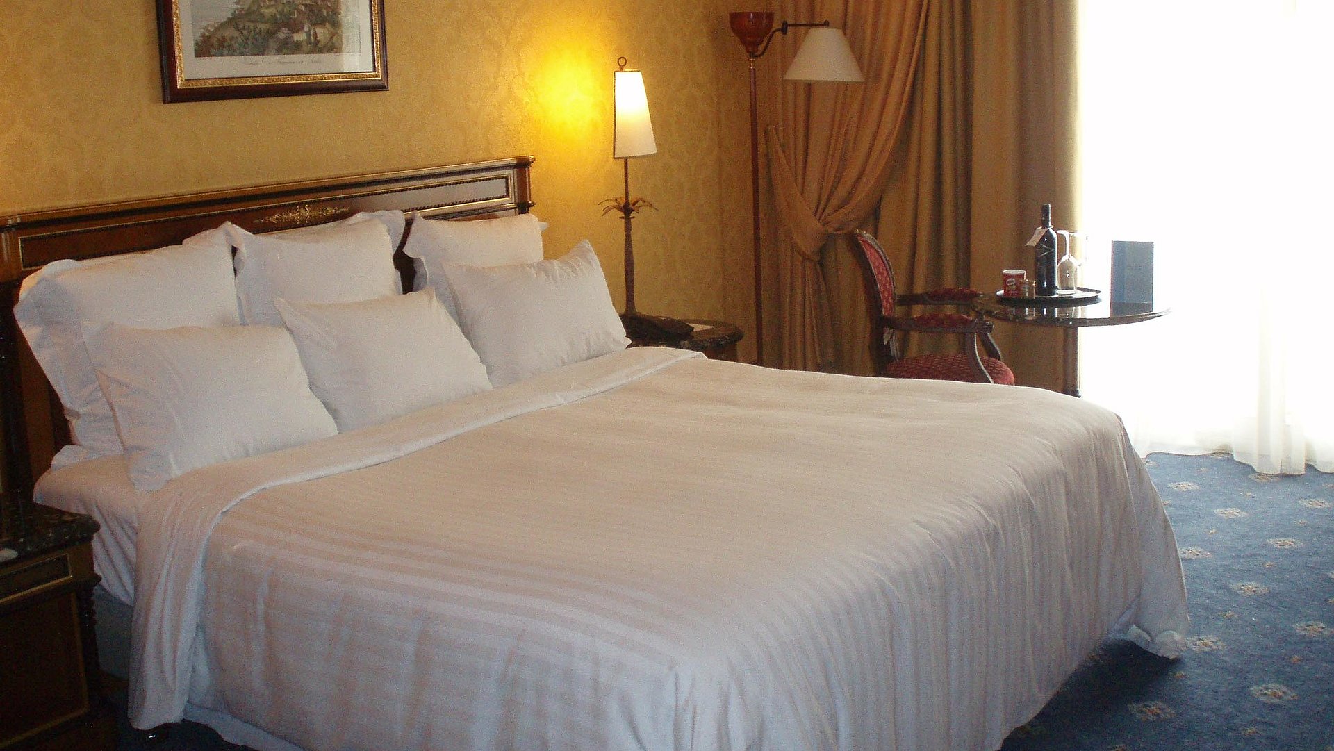 Hotels Für Gruppen in Oberbayern - sehr ordentliches Hotelzimmer mit großem Bett und warmer Nachtlampe wird durch weiße Gardinen durchleuchtet