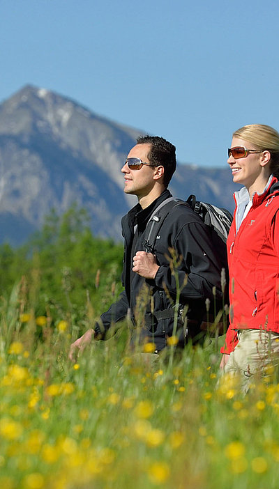 Wandern und Wanderurlaub in Oberbayern - zwei Partner auf Wanderung in Graslandschaft; Berge im Hintergrund