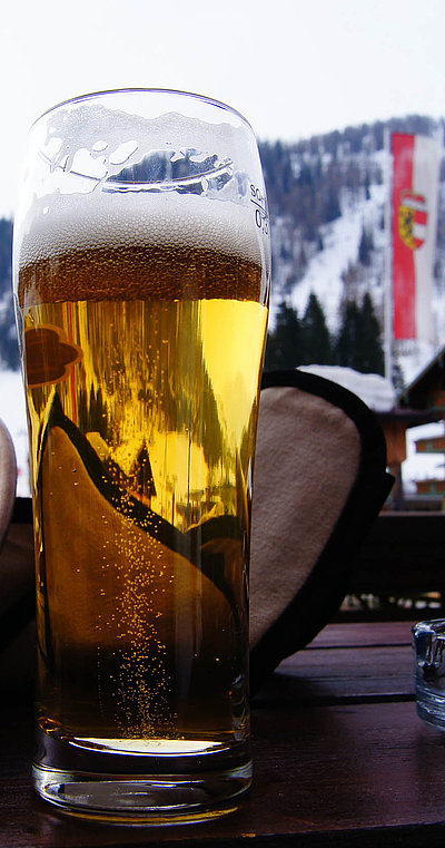 Biergärten im Ostallgäu - fast volles Bier auf einem Holztisch mit hügeliger Schneelandschaft im Hintergrund