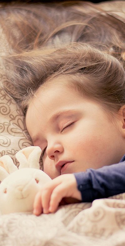 Kinderfreundliche Unterkünfte im Ostallgäu - kleines Mädchen mit Plüschhäschen liegt schlafend im Bett