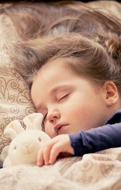 Kinderfreundliche Unterkünfte in Oberbayern - kleines Mädchen mit Plüschhäschen liegt schlafend im Bett