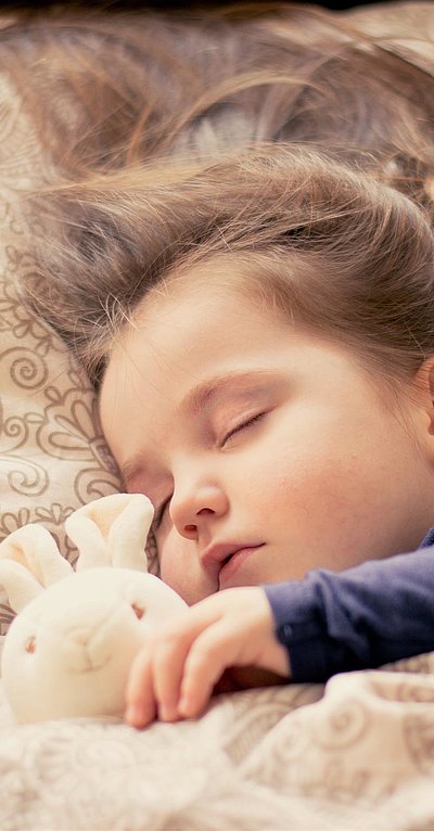 Kinderfreundliche Unterkunft im Oberallgäu - kleines Mädchen mit Plüschtierhäschen liegt schlafend im Bett
