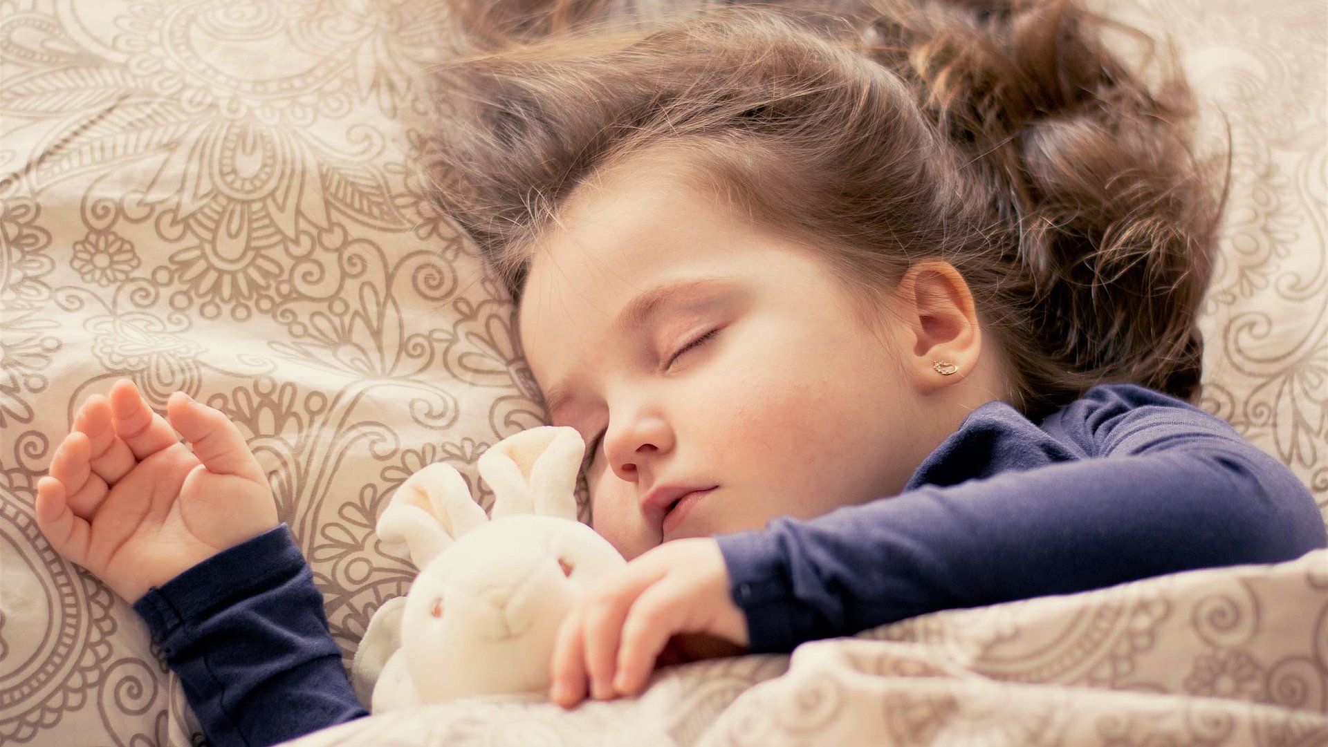 Kinderfreundliche Unterkünfte in Oberfranken - kleines Mädchen mit Plüschtierhäschen liegt schlafend im Bett 
