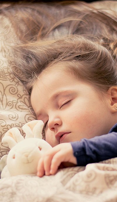 Kinderfreundliche Unterkunft in Kempten - kleines Mädchen mit Plüschtierhäschen liegt schlafend im Bett