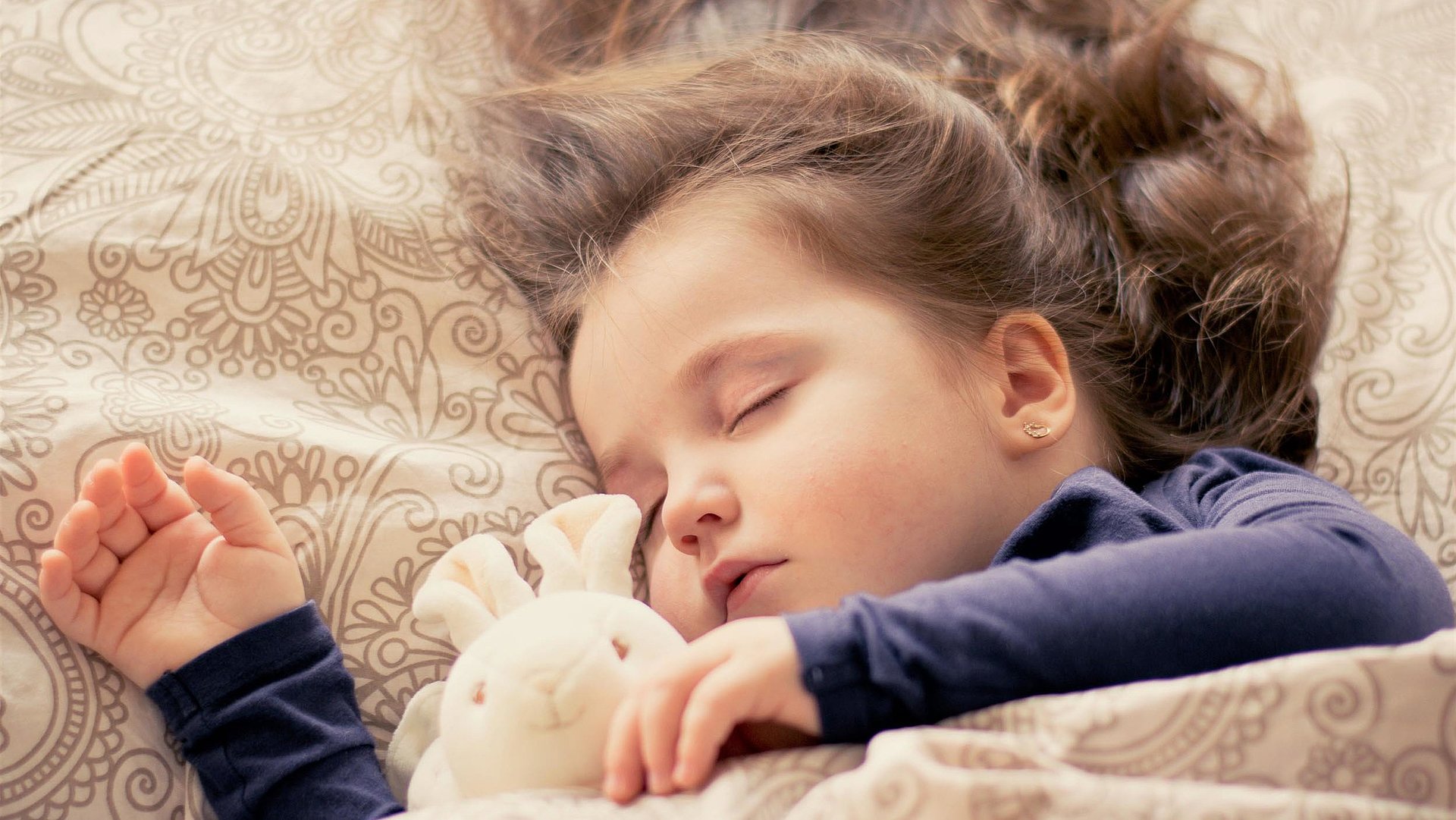 Kinderfreundliche Unterkunft in Ostbayern - kleines Mädchen mit Plüschhäschen liegt schlafend im Bett 