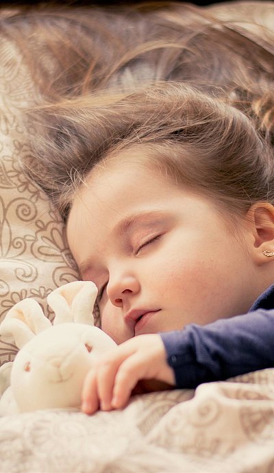 Kinderfreundliche Unterkünfte in Ostbayern - kleines Mädchen mit Plüschtierhäschen liegt schlafend im Bett 
