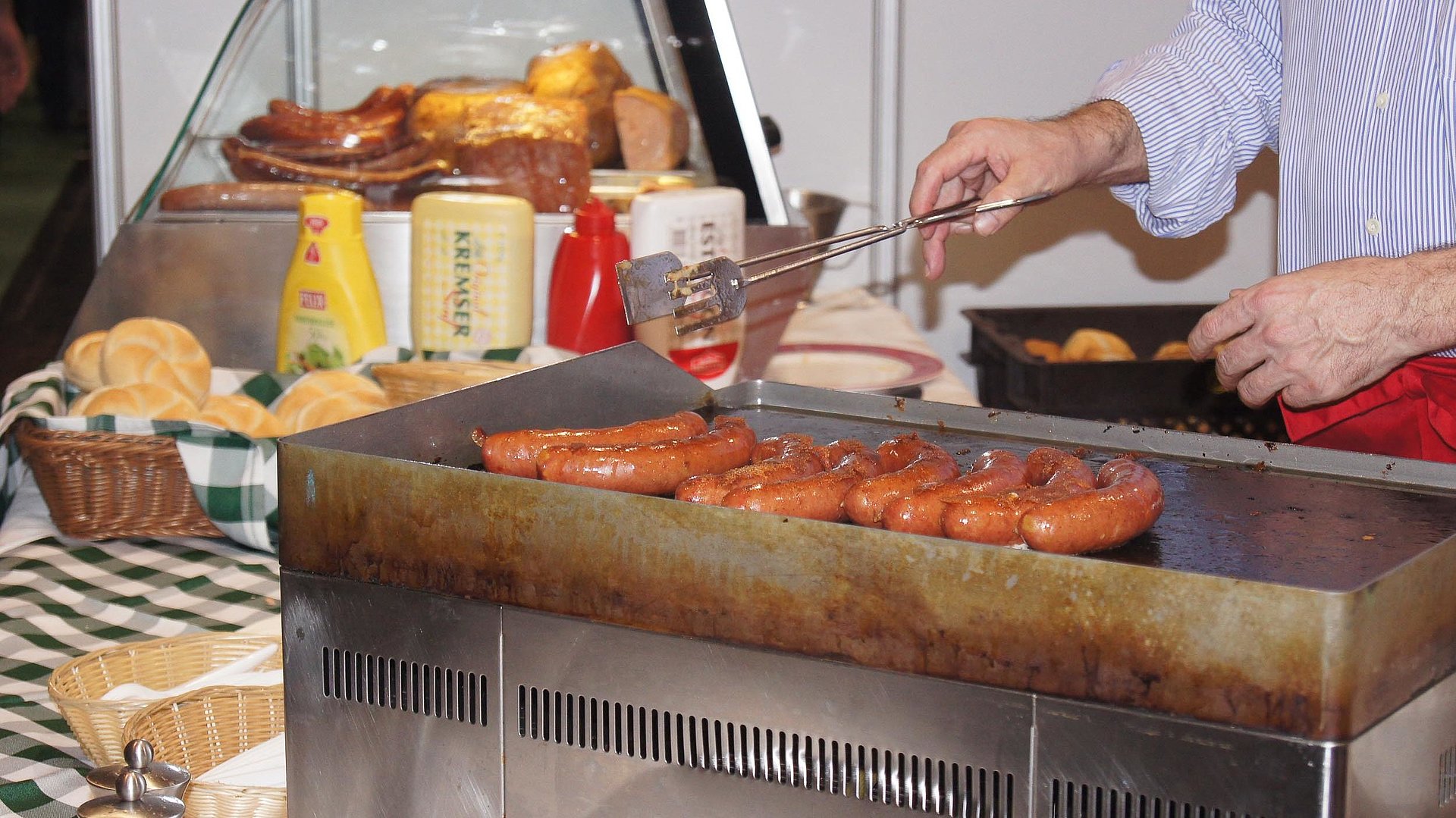 Gastronomie für Gruppen im Ostallgäu - Mann grillt soeben Würsten, im Hintergrund sind Brötchen und Soßen wie Ketchup und Senf