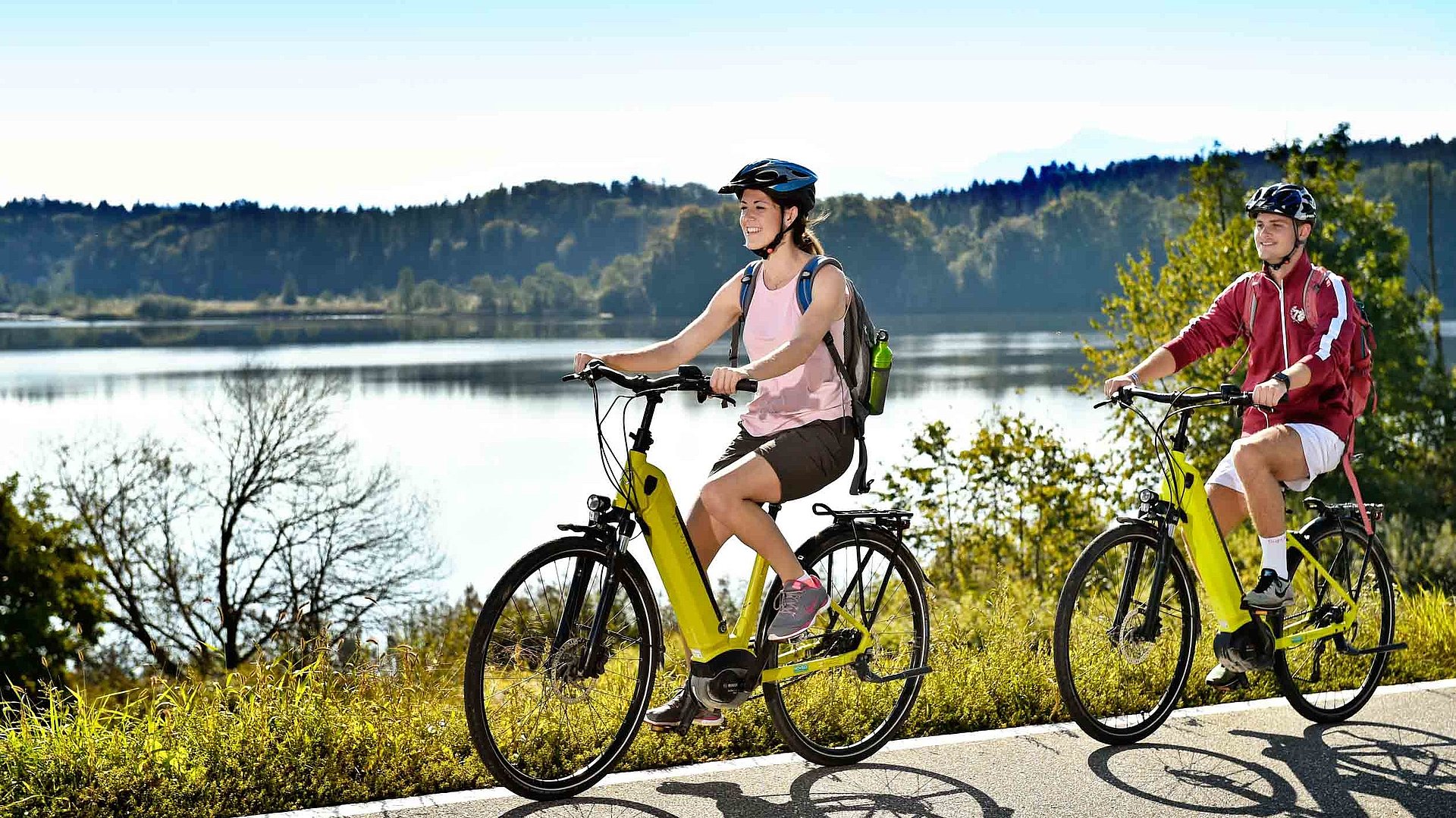 Freizeit und Sport in Mittelfranken - zwei Radfahrer mit E-Bike fahren auf Radweg bei sonnigem Wetter an einem See vorbei; Waldlandschaft im Hintergrund