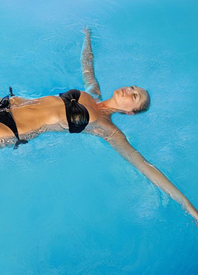 Wellness in Ostbayern - junge Frau im schwarzen Bikini liegt mit ausgestreckten Armen mit dem Rücken in einem Pool