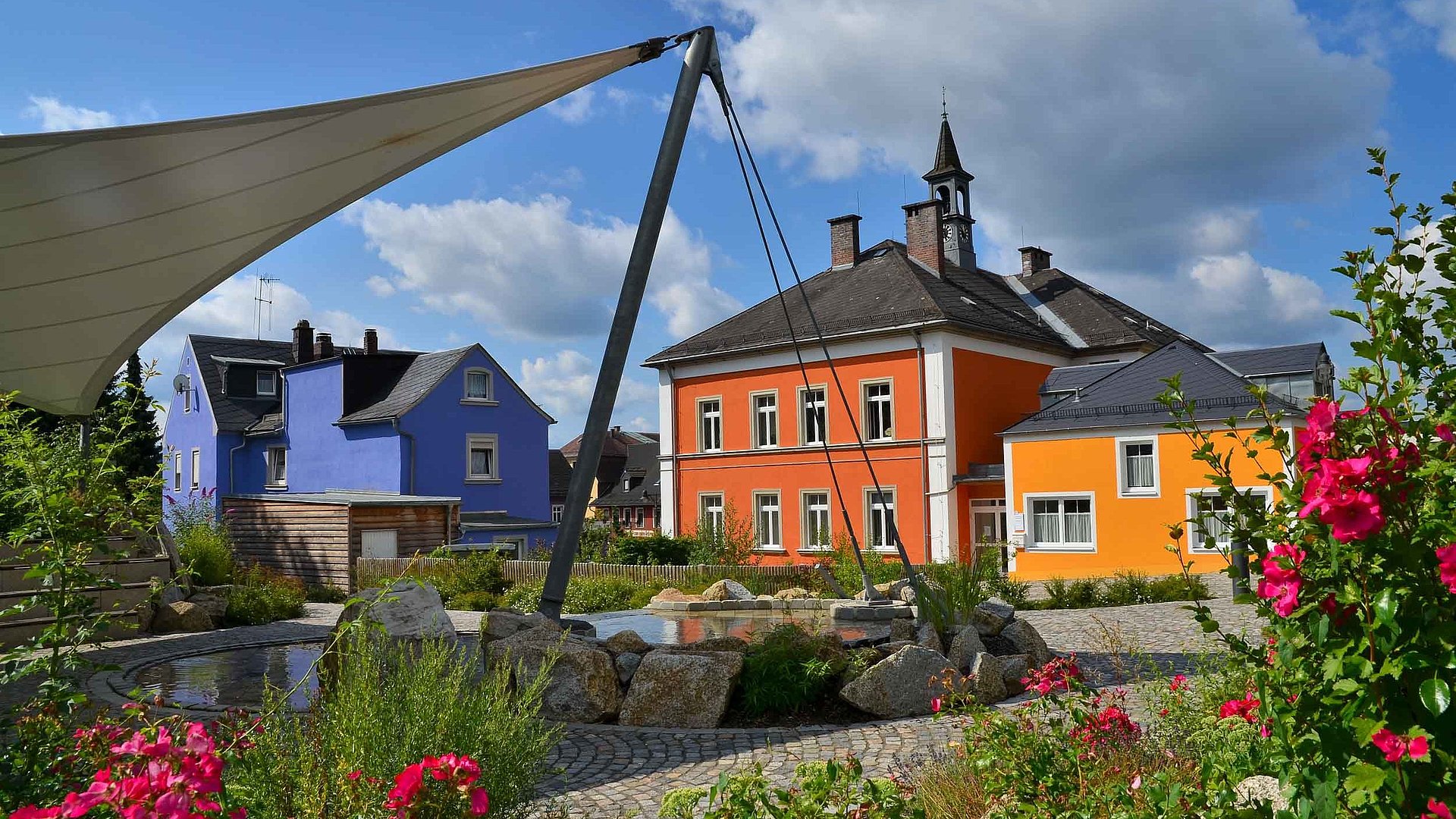 Pauschalangebote für Unterkünfte zu Feiertagen im Fichtelgebirge - Ortsmitte von Röslau bei schönem Wetter, linke Seite mit blauem Haus und rechte Seite ein großes oranges Haus
