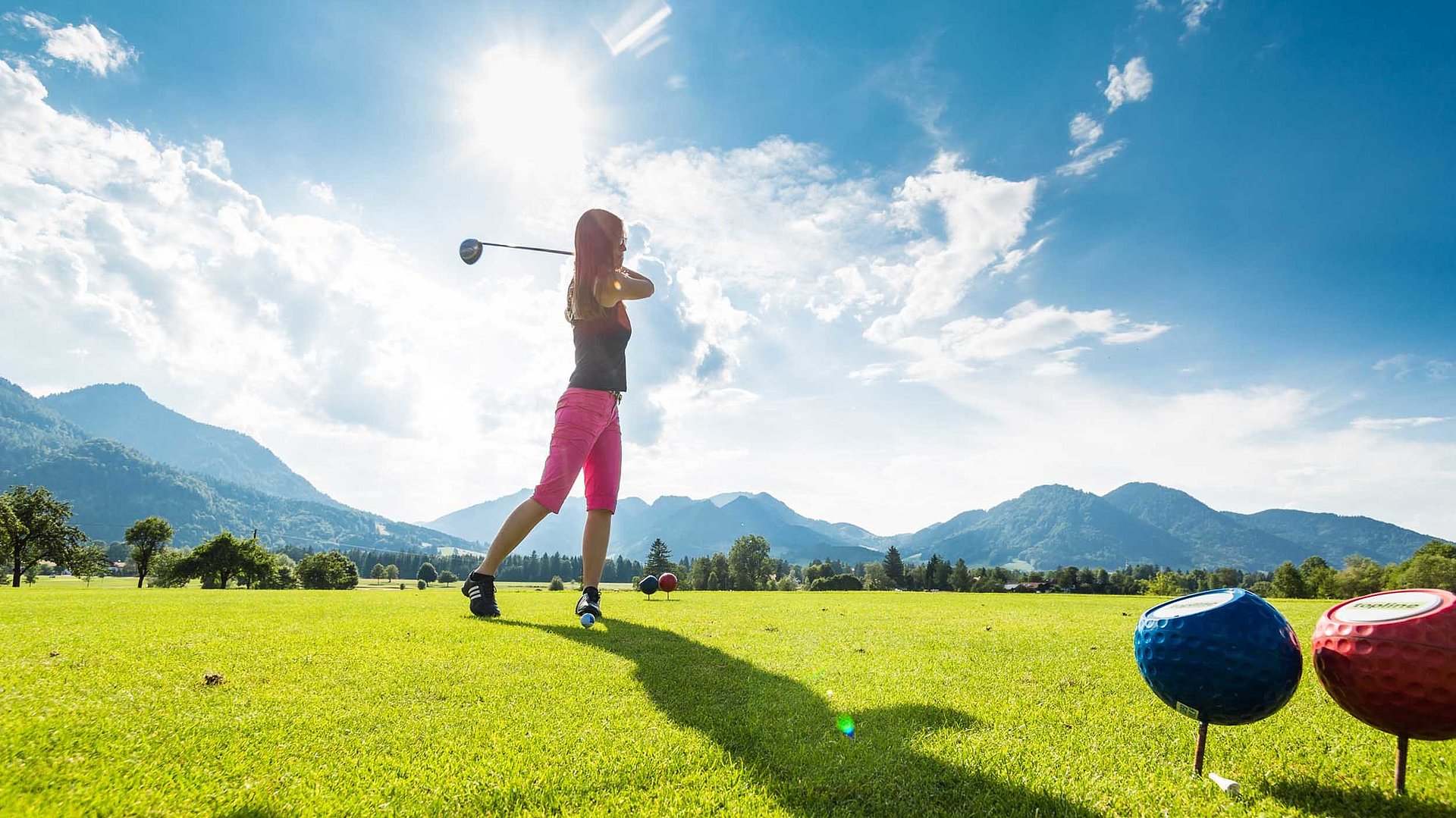 Golf im Oberallgäu - junge Frau macht grad ihren Abschlag, bei sonnigen Wetter mit Hügeln im Hintergrund