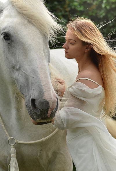 Urlaub auf dem Bauernhof in Mittelfranken - junge Frau mit langem blonden Haar und weißem Kleid streichelt weißes Pferd