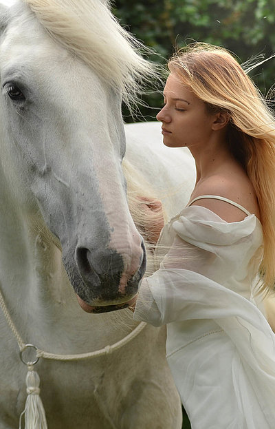 Reiten und Reiturlaub in Franken - junge Frau mit langem blonden Haar und weißem Kleid streichelt weißes Pferd