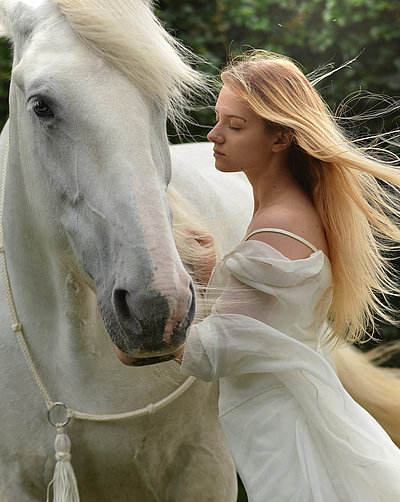 Urlaub auf dem Bauernhof im Fichtelgebirge - junge Frau mit langem blonden Haar und weißem Kleid streichelt weißes Pferd