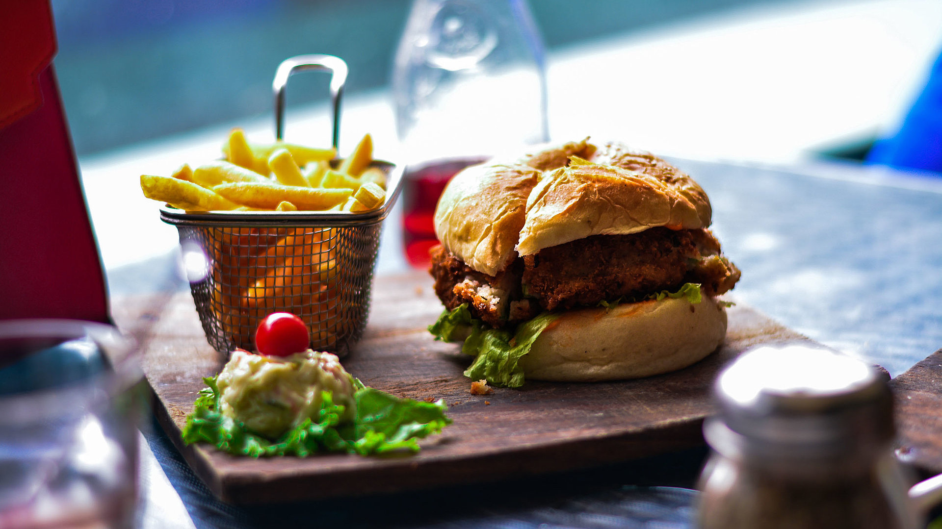 Internationale Gastronomie in Franken - im Restaurant; Burger, Pommes und Salat auf einem Holzbrett