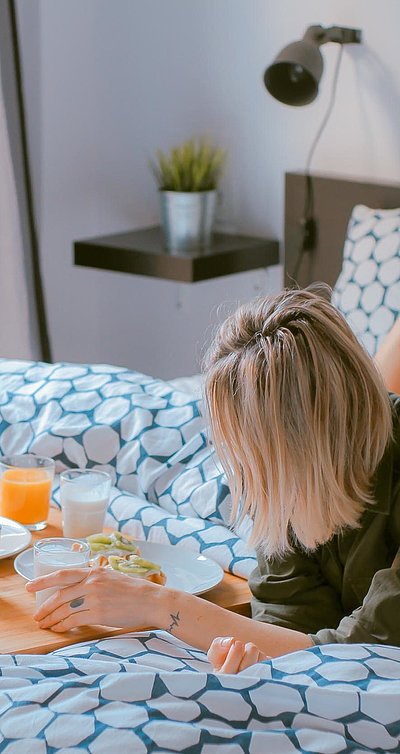 Übernachten im Video in Ostbayern - junge blonde Frau liegt im Bett neben einer Frühstücksplatte, gefüllt mit O-Saft, Milch und belegten Brötchen
