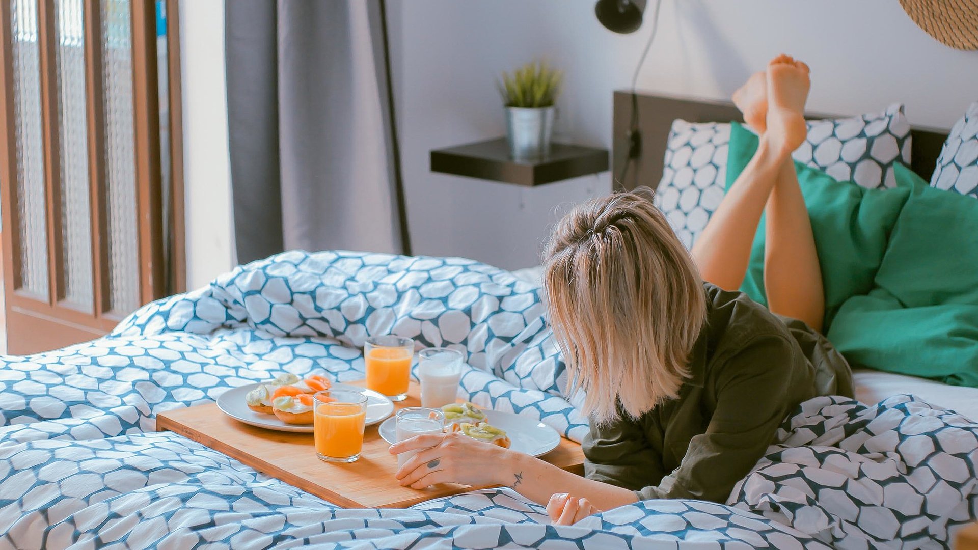 Ferienwohnungen und Appartements für Gruppen in Unterfranken -  junge blonde Frau liegt im Bett neben einer Frühstücksplatte, gefüllt mit O-Saft, Milch und belegten Brötchen