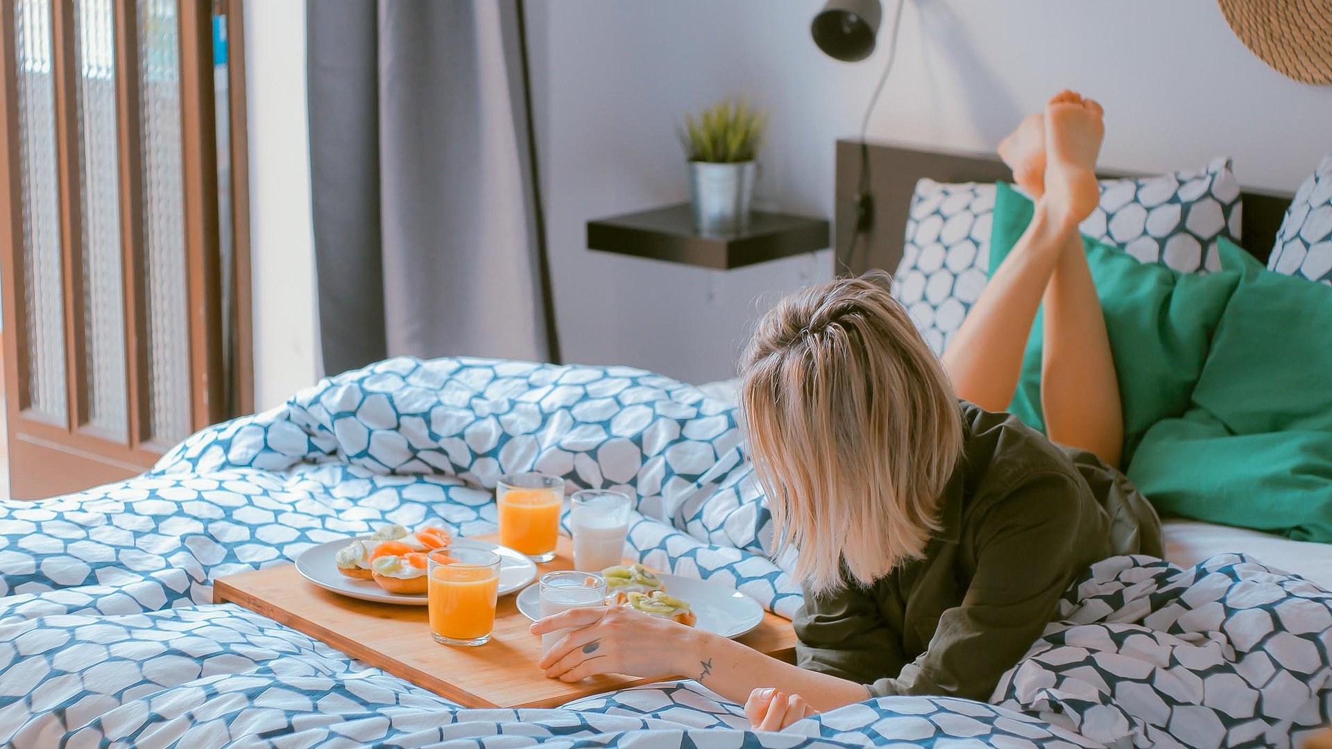 Unterkunft in Unterfranken - junge blonde Frau liegt im Bett neben einer Frühstücksplatte, gefüllt mit O-Saft, Milch und belegten Brötchen
