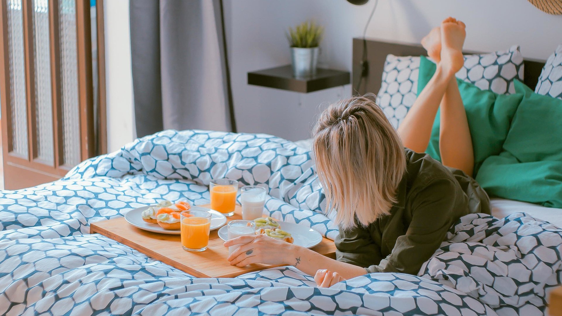 Übernachten Video in Franken - junge blonde Frau liegt im Bett neben einer Frühstücksplatte, gefüllt mit O-Saft, Milch und belegten Brötchen