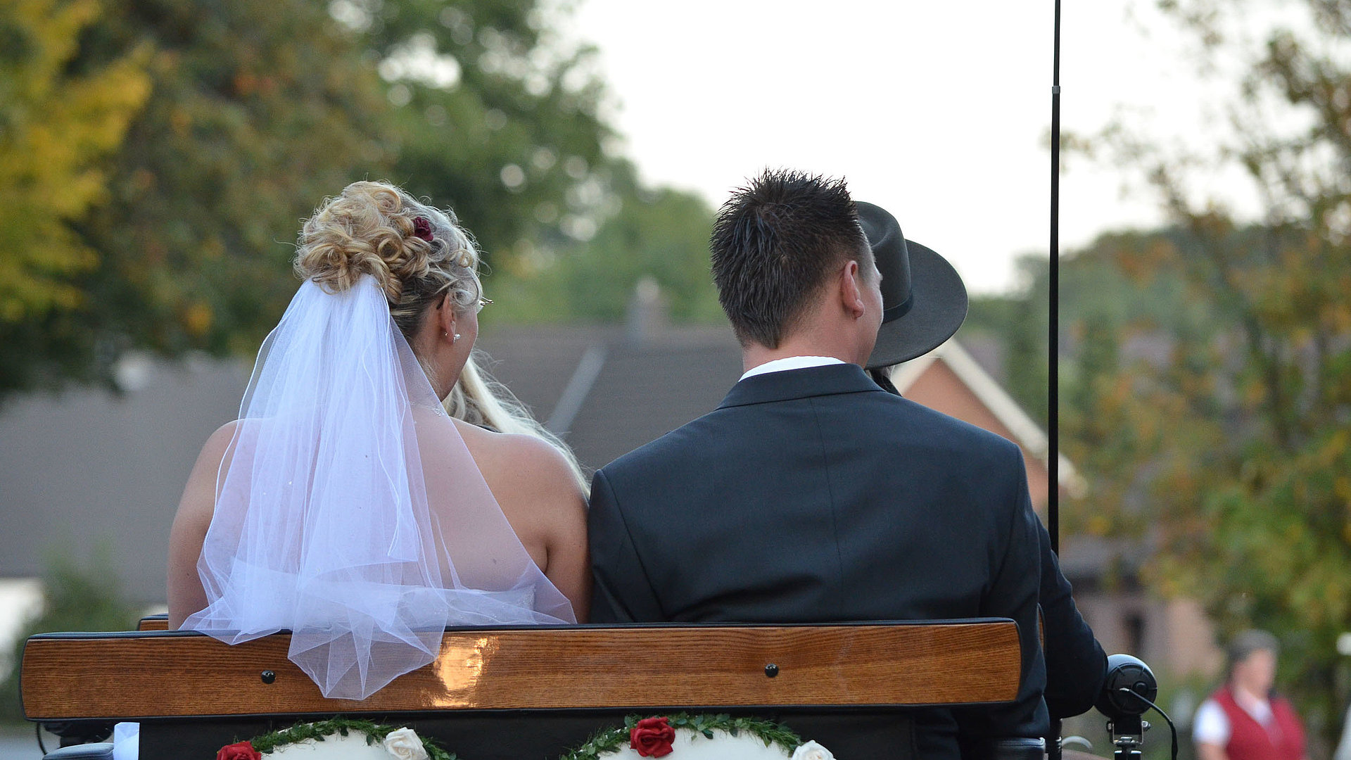 Heiraten in Oberfranken - Brautpaar sitzt auf einer Bank; mit Rücken zur Kamera und schauen auf das Fest