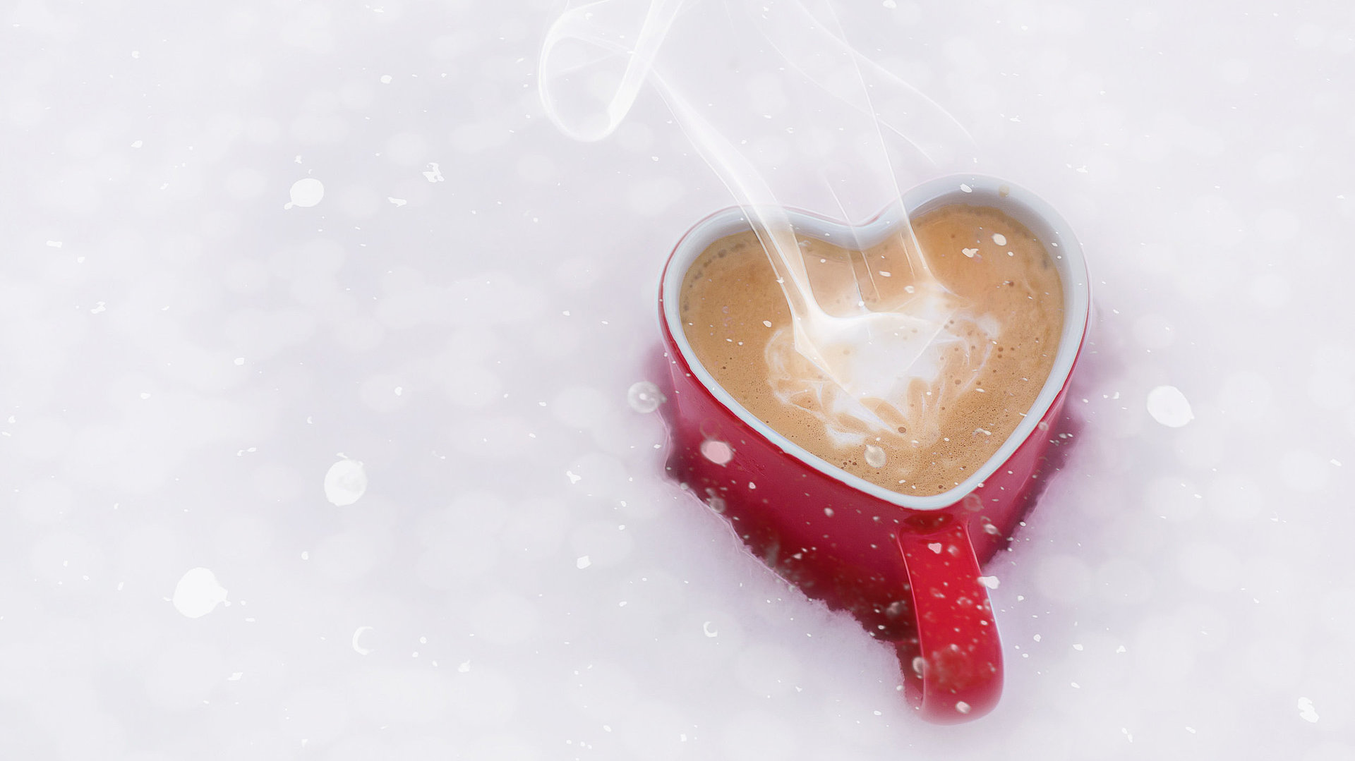Cafés in Oberbayern - Kaffeetasse in Herzform mit dampfendem Kaffee im Schnee
