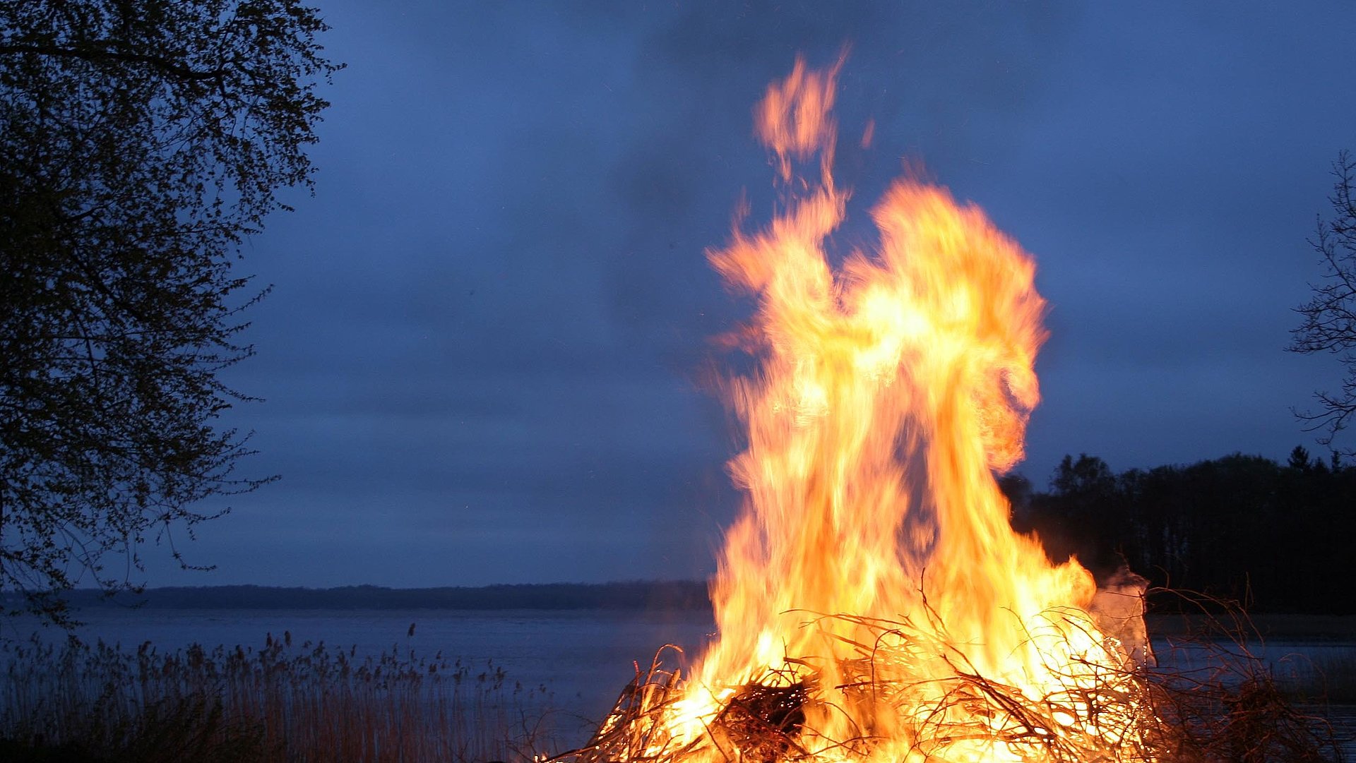 Camping in Unterfranken - Fokus auf großes Lagerfeuer in der Nacht am See