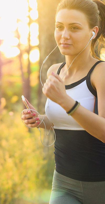 Outdoor-Freizeitangebote in Oberfranken - junge Frau mit Kopfhörern joggt im Wald bei Sonnenlicht